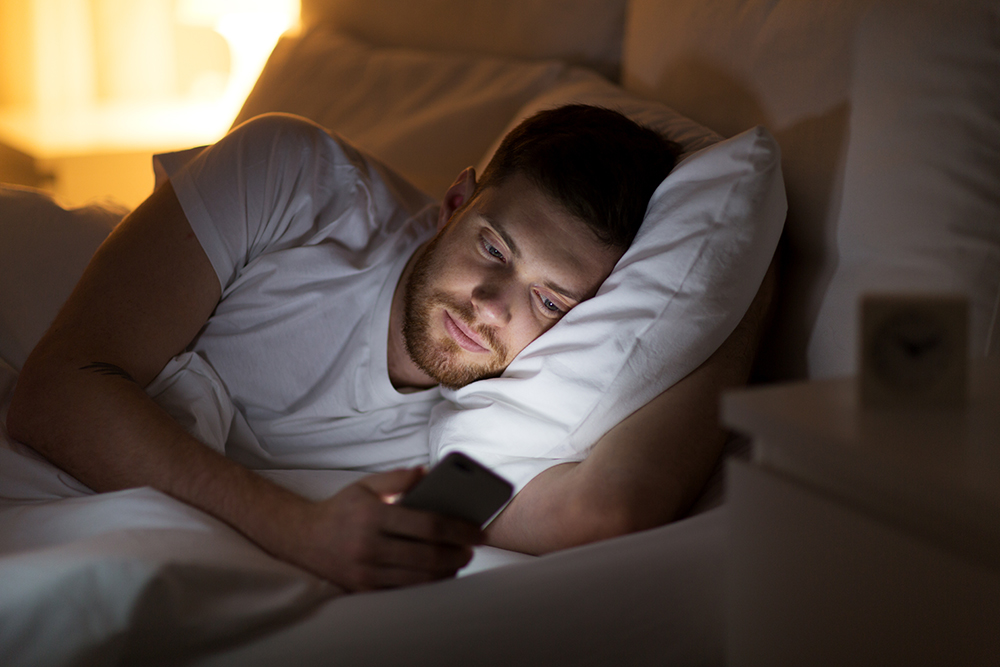 Man lying in bed scrolling on a smartphone.