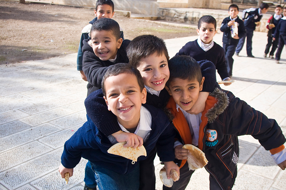 Three boys joyfully play together in the sand outdoors in Gaza, highlighting childhood innocence and friendship.